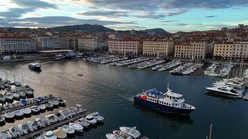 Aerial view of the Old Port of Marseille, France, showing rows of docked boats, colorful historic buildings, and a scenic ferry cutting through the calm harbor waters. Marseille, France. May 30th 2024 video