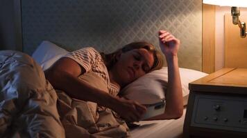 Young woman waking up at night and checking time on the smartphone looking upset video