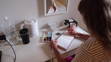 hobbies on the vacation. woman sitting at small table drawing using watercolor in hotel room video