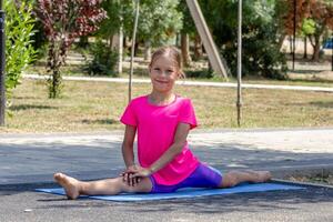 A child sitting on the pavement with legs extended straight forward and backward in a full front split, show flexibility and stretch photo