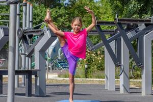 A child balancing on one leg while holding the other leg raised high, demonstrating flexibility and balance through a stretching pose photo