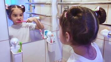 Adorable little girl brushes her teeth in the bathroom in front of the mirror video