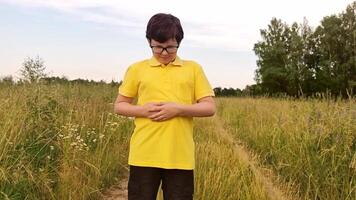 A boy stands in a field in the summer, holds his hands on his stomach. video