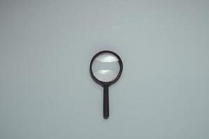 Classic magnifying glass with black handle and clear lens, centered vertically on smooth, muted blue. Ideal for search, investigation, discovery, research, and analysis. photo