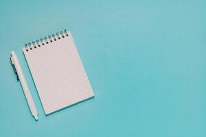 Blank grid notepad and white pen neatly arranged on vibrant blue. Ideal for planning, writing, study, note-taking, and professional workspace. photo