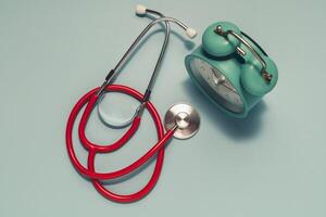 Vibrant red stethoscope and teal vintage alarm clock on light blue. Highlights the importance of regular medical check-ups and efficient health appointment management. photo