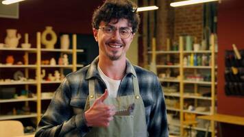 Caucasian man smiling in pottery workshop cheerful happy male potter artisan craftsman guy small business owner sculptor showing thumb up gesture recommend craft store handmade hobby ceramic sculpture video