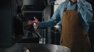Caucasian man worker in coffee roasted fabric industry working stand near roasting machine with cacao beans mixing talking mobile phone call male small business owner talk communicate with smartphone video