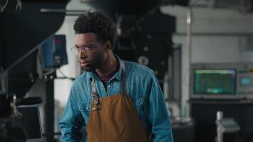 African American man worker in coffee roasting fabric checking roasted cocoa machine smiling at camera posing crossed hands male guy wearing apron working in coffehouse distribution organic production video