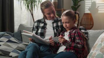 Caucasian mother and daughter child girl kid on sofa at home girl using smartphone rejecting book offered by mom digital addiction family education mobile phone technology conflict parenting problem video