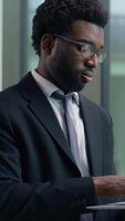 African American businessman male business man in office looking out window typing laptop smiling happy working at workplace using corporate software chatting internet browsing analyzing online data video