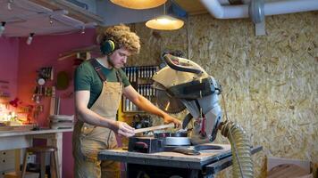 Young attentive woodworker checks wooden beam, cut it on miter saw in workshop. Records measurements video