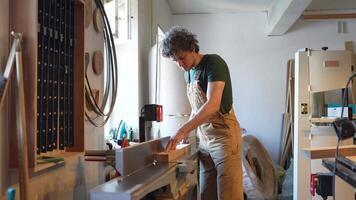Young woodworker works with electric jointer, honing wooden block in workshop. Final sanding polish video