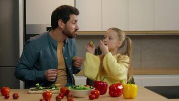 Happy Caucasian family cooking together at kitchen carefree child girl daughter kid playing fun with father making cucumber slices glasses cover eyes with vegetable circles laughing smiling eating video