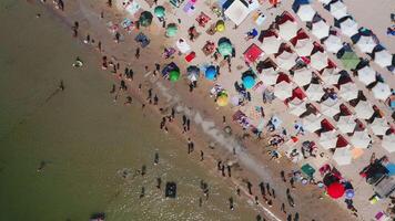 Aerial view of the city beach on a hot summer day. Sun umbrellas are on the white sand. People are relaxing and sunbathing on the beach on a summer day by the ocean. video