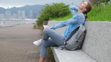 Caucasian woman on city embankment sitting on the bench and looking at view, summer vacation in city video