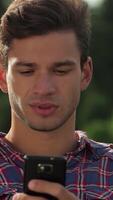 A young man captivated by his smartphone in a lively park video