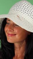 Charming woman beaming at the camera while adjusting her stylish white hat video