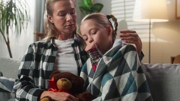 Caucasian family cuddling at home caring mother comforting sick daughter coughing ill wrapped in blanket on couch sad kid child girl hugging Teddy Bear cough sick love support medicine health problem video