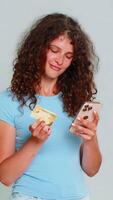 Woman happily smiling holding credit card, smartphone after making successful online order purchase. Girl on gray background expresses positive satisfied buyer emotion using mobile phone for shopping video