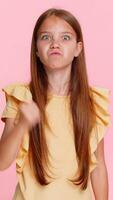 Young child girl raises fist with angry expression, pretending to threaten someone in a humorous way, showing dissatisfaction frustration. School kid isolated on pink background expressive energetic video