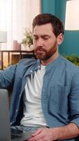 Young man at home smiling with satisfaction while closing laptop after completing work. Caucasian guy sitting on sofa, feeling accomplished, relieved, and happy about finishing tasks or projects video
