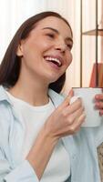 Young happy woman at home holding cup of tea inhaling aroma happily, relaxing and enjoying peaceful quiet moment. Caucasian girl on sofa satisfied, expressing calm emotions, comfort, tranquility video