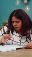 Indian woman at home writes idea in notebook crosses it out then retries showing determination to find solution. Arabian girl at table edits notes seeking creative answer with persistence and focus. video