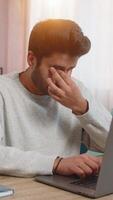 Young Indian man freelancer working on laptop, looking tired, rubbing eyes while sitting at table on sofa in living room at home. Arabian guy, a workaholic, continues his tasks, clearly exhausted. video