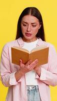 Young woman reading book with wide open eyes amazed expression, deeply intrigued by thrilling and surprising plot. Girl on yellow background emotionally reacts to intense captivating story development video