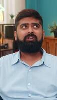 Indian man at home rolls eyes showing ironic reaction during smartphone chat dismissing odd comment. Arabian guy on sofa shows sarcasm disbelief slight head tilt expresses annoyance humorous attitude. video