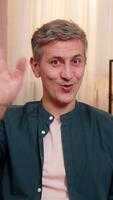 Young happy man at home pointing at camera with smile during call greeting excitedly. Caucasian guy on sofa shows joy happy energy and enthusiasm, saying hello with expressive friendly attitude video