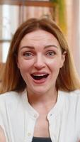 Middle-aged woman looks at camera on home sofa with surprise, saying wow and reacting with big emotion. Young adult girl shows amazement and visible shock, overwhelmed by unexpected moment or news. video