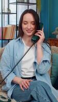 Young woman at home surprisedly answering vintage wired telephone from 90s, nostalgically smiling and listening pleasant memories. Caucasian girl happily experiencing emotional nostalgic moment video