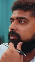 Indian man at home holds pen by face gazing forward carefully planning tasks with focused mind now. Close-up Arabian guy contemplates goals twirling pen thinking through next moves and strategic ideas video