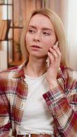 Young adult woman rejects annoying call on smartphone while sitting on sofa, waving hand with refusal. Girl reacts with frustration to spam or scam caller, expressing disagreement with body language. video