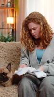 Young angry Caucasian redhead woman tosses bills on home sofa, expressing nervous frustration and emotional stress. Pug dog observes her reaction with surprised look, sensing mood and confusion. video