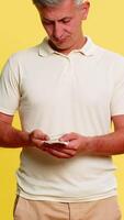 Middle-aged man pulling out few dollar bills from pocket spreading hands with helpless expression symbolizing financial trouble bankruptcy or debt. Young guy showing poor emotion on yellow background. video