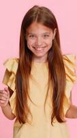 Young child girl raises hands with a victory win gesture, smiling brightly and celebrating a joyful success moment. School kid isolated on pink background, full of cheerful energy and positive emotion video