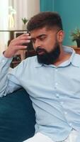 Indian man at home slaps forehead facepalm after smartphone error looks disappointed regretful frustrated. Arabian guy on sofa lowers head grimaces shows guilt mistake reaction stress negative mood. video