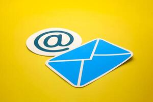 Paper letter and at sign on yellow background, with copy space. Business concepts of online contact channels, and electronic mail inbox notifications. photo