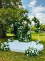 In a beautiful park, there is a stunning wedding arch that is elegantly decorated with gorgeous white flowers and lush greenery, creating a picturesque setting for a lovely celebration photo