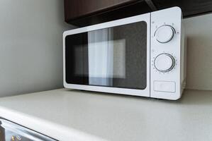 A gleaming white microwave oven significantly enhances the kitchens stylish and modern aesthetic, perfectly matching and complementing the coordinated white countertop where it is placed photo
