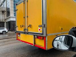 This closeup shows a vibrant yellow delivery truck with bright reflective markings in a bustling urban setting, highlighting its essential role in the citys logistics and transportation photo