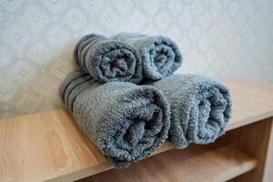 Three neatly rolled towels are carefully arranged on a beautiful wooden shelf, beautifully adding warmth and stylish flair to your bathroom decor, enhancing its overall aesthetic appeal photo