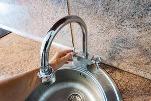 A person skillfully opens a kitchen sink faucet, which is a vital and essential fixture that dispenses water and other liquids necessary for a wide variety of household tasks and activities photo