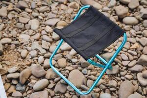 A compact, lightweight folding chair is positioned on top of a carefully arranged pile of assorted rocks, creating a striking contrast between the chairs design and the rugged surface photo