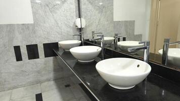 Modern white ceramic sinks with chrome faucets on a black countertop in a clean public restroom, reflected in a wall mirror. Minimalist and functional bathroom interior design. photo