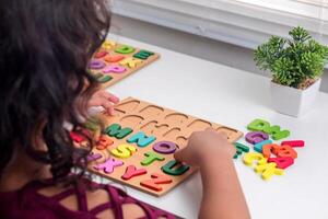 A little Asian girl plays with wooden alphabet letters puzzle on the table photo