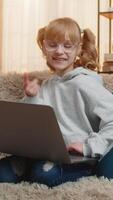 Young teenager girl rests at home with laptop, making a fun call online and laughing at her own reflections making silly faces. Child kid waves hi in excited joy and saying I am so funny look video